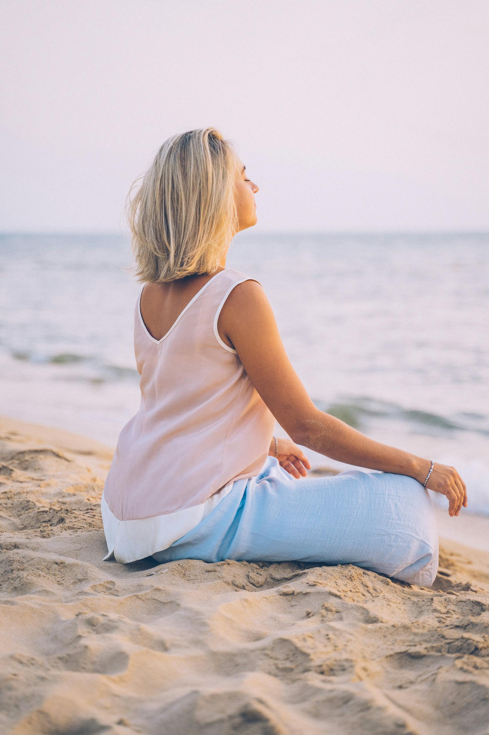 A serene moment of a woman practicing mindfulness meditation by the beach at sunset.